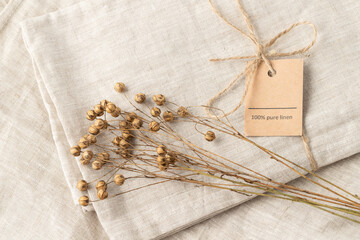 Dried flax plant bunch on folded natural linen fabric with rope and text 100% Pure Linen.