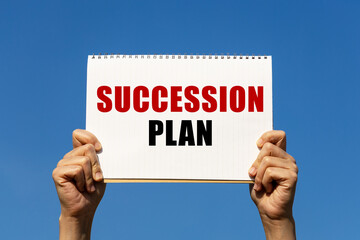 Succession plan text on notebook paper held by 2 hands with isolated blue sky background. This message can be used as business concept about succession plan.