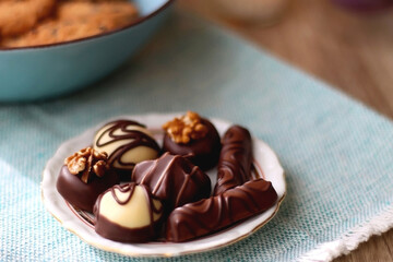Plate of chocolate pralines, bowl of cookies, cups of tea, glasses of juice and lit candles on the table. Selective focus.
