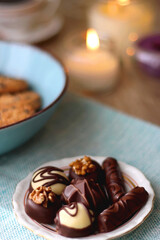 Plate of chocolate pralines, bowl of cookies, cups of tea, glasses of juice and lit candles on the table. Selective focus.
