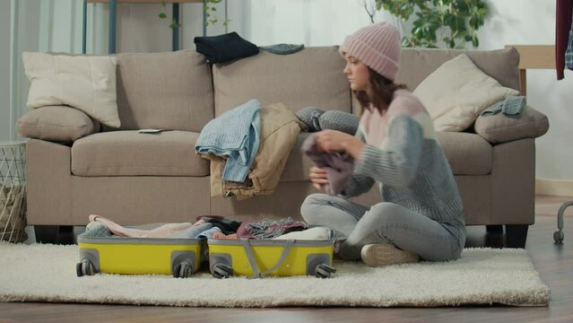 A Serious Young Woman Traveler in a Hat Gathers Clothes for a Trip, Packs Things into a Suitcase at Home. Winter Adventures. Travel Planning.