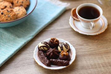 Plate of chocolate pralines, bowl of cookies, cups of tea, glasses of juice and lit candles on the table. Selective focus.