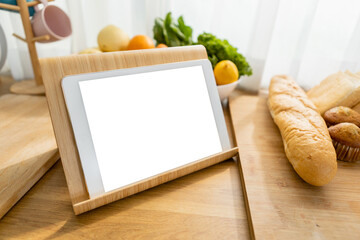 Tablet white screen on kitchen table with Vegetables, fruits and bread. Clipping path. Mockup display empty space use for graphic advertising text. Display live food online media.