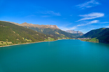 Fototapeta premium Aerial view of lake (Reschensee). Large reservoir surrounded by mountains at sunny noon. Recreation area for tourists and sportsmen. Italy, Vinschgau, Reschen.