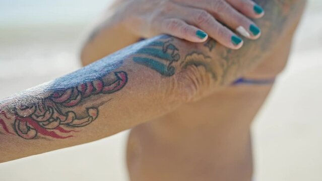 Middle age grey-haired woman tourist wearing bikini applying sunscreen on arm at beach