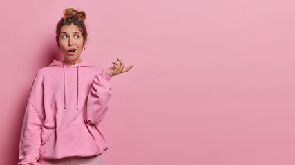 Horizontal shot of confused hesitant woman with hair combed in bun shrugs shoulders keeps palm...