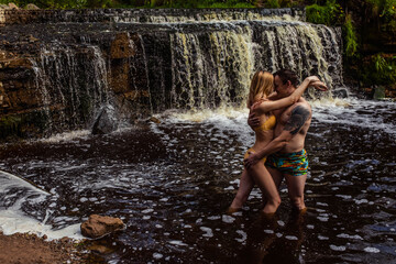 Fototapeta na wymiar Beautiful couple in waterfall hugging and kissing