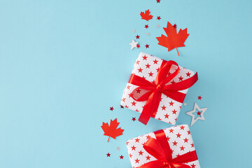 Symbolic Gifts for Celebrating Canada Day. Top view flat lay of patriotic gift boxes, red maple leaves, star-shaped confetti on light blue background with empty space for text or advert