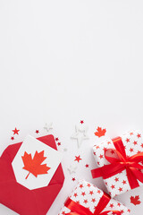 Canada Day gift theme concept. Top view vertical flat lay of envelope, greeting card, gift boxes, red maple leaves, event confetti on white background with empty space for text or ads