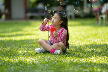 Outdoors portrait of cute Asian girl blowing soap bubbles on a green lawn.