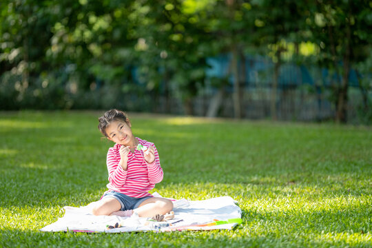 Outdoors portrait of cute Asian little girl painting a doll made of plaster on a green lawn.
