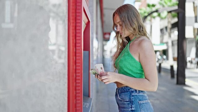 Young blonde woman holding israel shekels banknotes of cash machine at street
