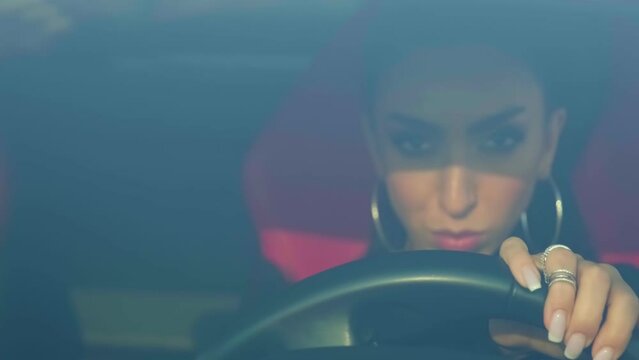 Young brunette in evening makeup and overalls behind the wheel of a premium sports car
