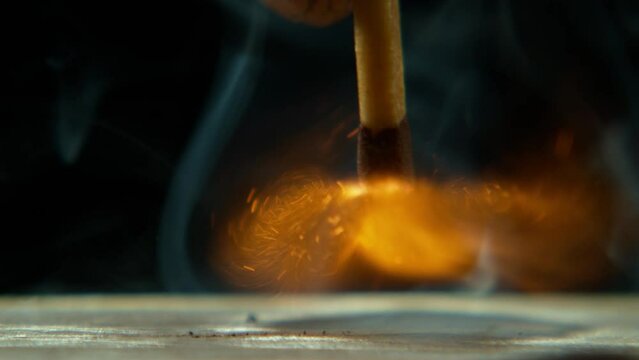 Match, flame strike and hand with matchbox stroke with sparks, fire and closeup. Dark, light and heat with smoke and black background with power outage and flames from burning wood and blackout