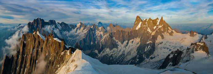 A panoramic view of the peaks and glaciers of the Mont Blanc massif at sunset. The sharp granite peaks  are illuminated by the evening sun.