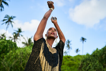 Epatage lgbtq black male posing with hands up on camera on scenic palm tree location. Non-binary...