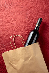 Paper shopping bag with a bottle of red wine on a textured red background.
