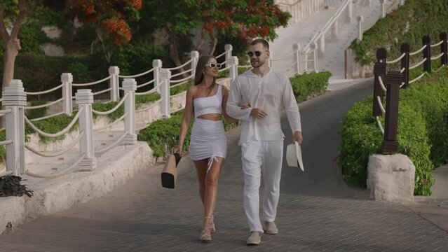 A beautiful couple of young people are walking around the territory of a modern luxury resort. A man and a woman in sunglasses and white clothes enjoy their holiday in Egypt.