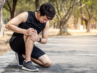 Athlete man feeling knee pain or rheumatoid arthritis while doing outdoor workout. Asian male...