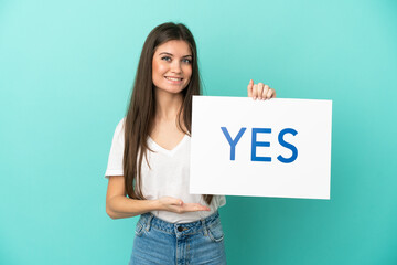 Young caucasian woman isolated on blue background holding a placard with text YES with happy...