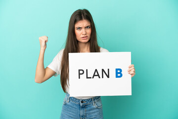 Young caucasian woman isolated on blue background holding a placard with the message PLAN B and...