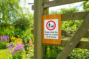 Dogs must be kept on lead sign seen attached to a garden gate leading to a secrete garden located at an old English churchyard.