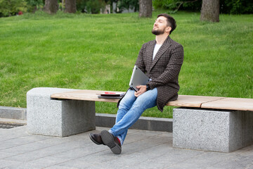 Obraz premium Successful businessman sits on a city bench and is engaged in business with documents and laptop