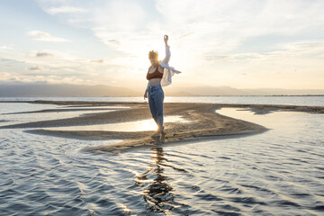 woman on the beach dancing at sunset in backlight with the sun behind in shadow, woman on vacation walking on the sand with golden water reflections from the sun at sunset, backlighting in the golden 