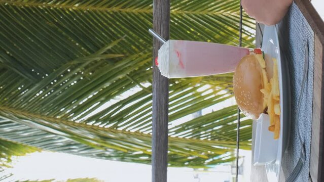 Vertical video. Cute little girl eating french fries while sitting on a terrace of cafe or a restaurant on summer vacation. Tropical travel lifestyle