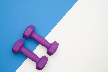 The layout of two rubberized dumbbells of 2 kg of purple color on a blue-white background, top view. Sports training