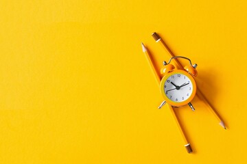 Orange alarm clock with pencils on orange background. The concept of awakening, work time, training...