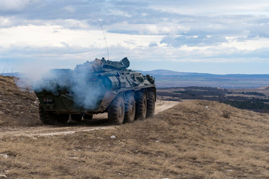 A BTR-80 armored personnel carrier in green camouflage is driving on a barren winter hill