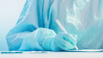 Medical documentation. Doctor paperwork. Healthcare professional worker hand in protective rubber glove writing diagnosis on white table on blue background.
