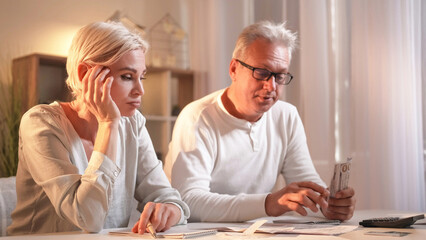 Family finance. Budget problems. Unhappy married man woman arranging counting money sitting table in light shadow room interior.