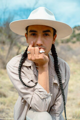 Fashionable queer Mexican native person in hat and jewelry outdoors in the desert - obrazy, fototapety, plakaty