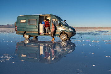 A family in a 4x4 camper van in a salt flat with water that generates a perfect reflection © JoseMaria