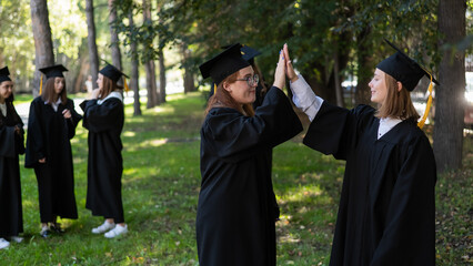 Group of happy students in graduation gowns outdoors. A young girl with a diploma in her hands in the foreground.