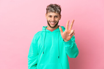 Young handsome caucasian man isolated on pink background happy and counting three with fingers