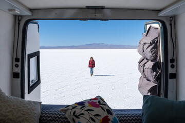 A girl walking in a salt flat seen from inside a 4x4 campervan.