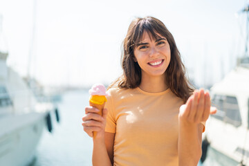 Young woman with a cornet ice cream at outdoors inviting to come with hand. Happy that you came