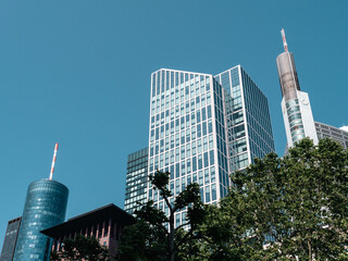 Frankfurt Germany - Low angle view of office building skyscraper next to contemporary high rise structures with glass mirrored walls and illuminated lights in Frankfurt city against cloudless blue sky