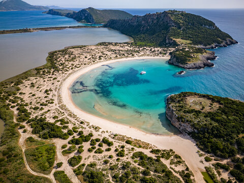 Aerial View Of Voidokilia Beach On Peloponnese In Messinia / Greece With Clear Blue Water And Catamaran Sailing Boat In The Bay