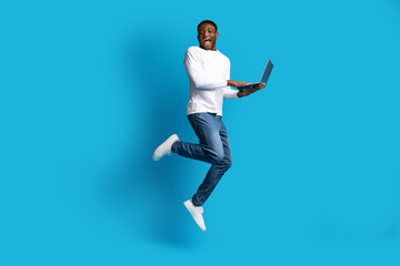 Happy black guy jumping with laptop in his hands
