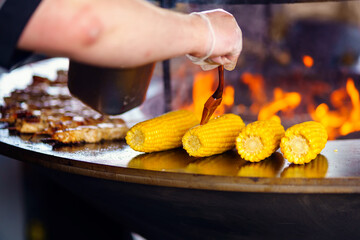 The cook of a street restaurant greases corn with oil, which is baked over an open fire