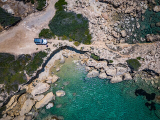 Aerial view of a white off-roader on a road trip on the coast of Greece with turquoise, clear water...