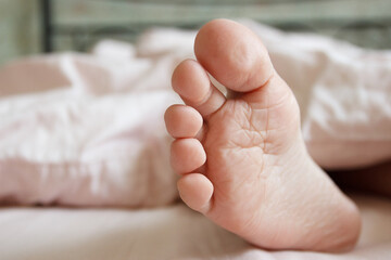Feet under a light blanket on the bed. Concept of health