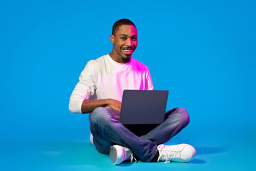 Happy young black man using laptop on blue background