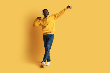 Fototapeta premium Positive black guy taking selfie on smartphone, using headphones