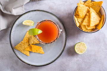 Michelada cocktail with tomato juice, beer and lime in a glass and nachos top view