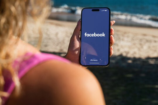 Girl on the beach holding a iPhone 14 Pro smartphone with Facebook app on the screen. Rio de Janeiro, RJ, Brazil. June 2023